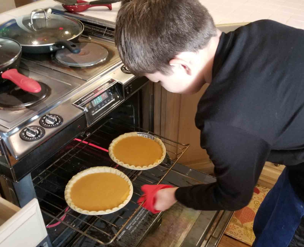 A child with autism takes pumpkin pies out of the oven during an ABA therapy life skills session