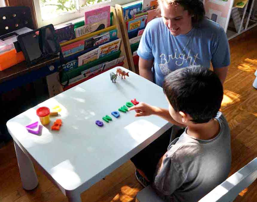 A child with autism and therapist work at a table with letter toys during an ABA therapy session