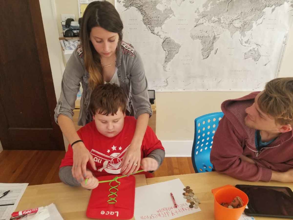 An ABA therapy technician helps a child with autism to learn to tie laces