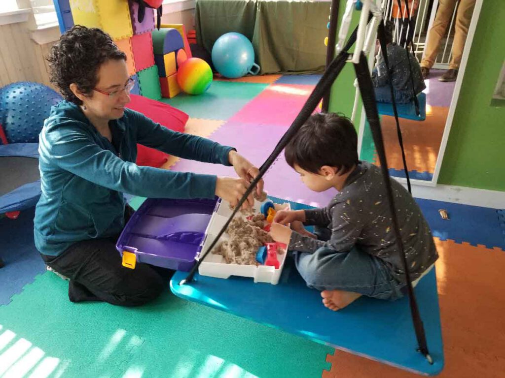 A therapist guiding a young child through a sensory play activity during pediatric occupational therapy.