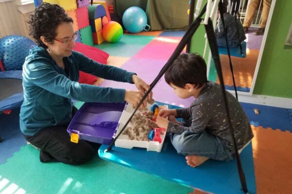 A therapist guiding a young child through a sensory play activity during pediatric occupational therapy.