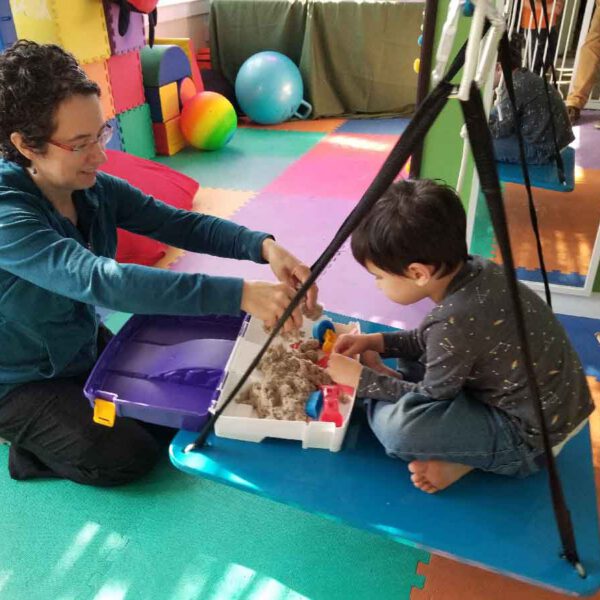 A therapist guiding a young child through a sensory play activity during pediatric occupational therapy.