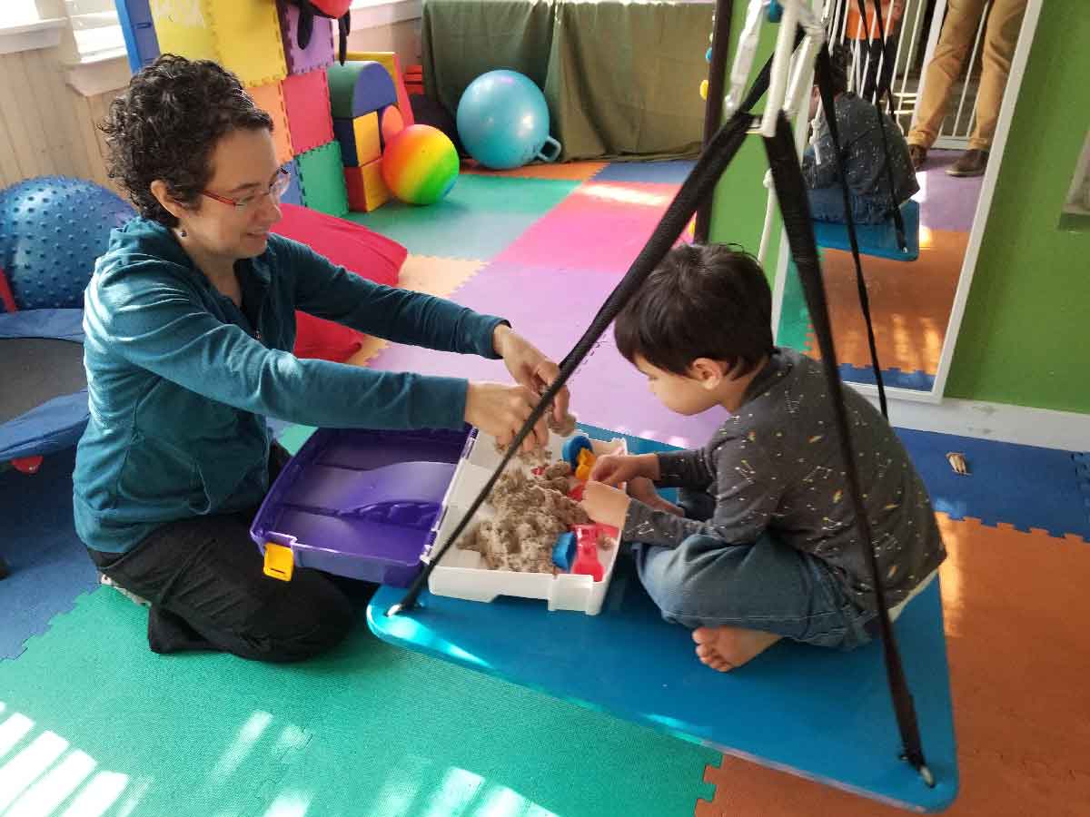 A therapist guiding a young child through a sensory play activity during pediatric occupational therapy.