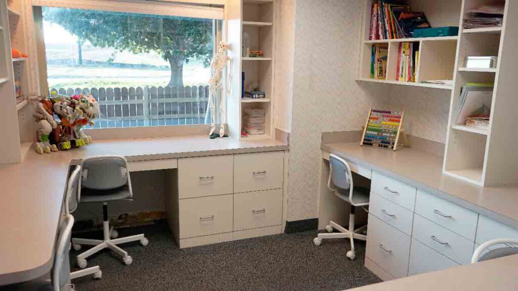 Structured Discrete Trial Training (DTT) room at Bright Mosaic on Bonnie Brae St. featuring individual therapy desks, organized toy storage, and a large window for a bright, focused ABA learning environment.