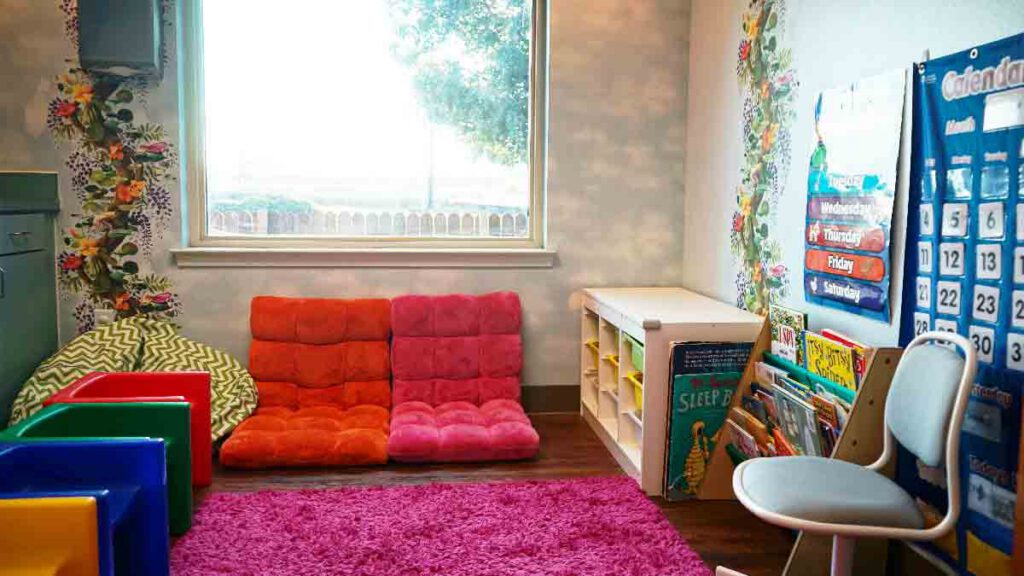 Classroom for circle time at Bright Mosaic on Bonnie Brae St., featuring a pink shaggy rug, floor seating, a calendar chart, and a bookshelf for group story time and school readiness skills.