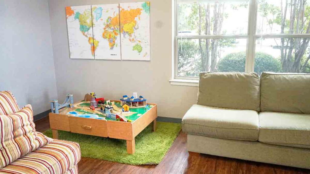 Sunlit indoor collaborative play area at Bright Mosaic on Bonnie Brae St., featuring comfortable sofas, a wooden train table, and a colorful world map for child-led social interaction and ABA therapy.