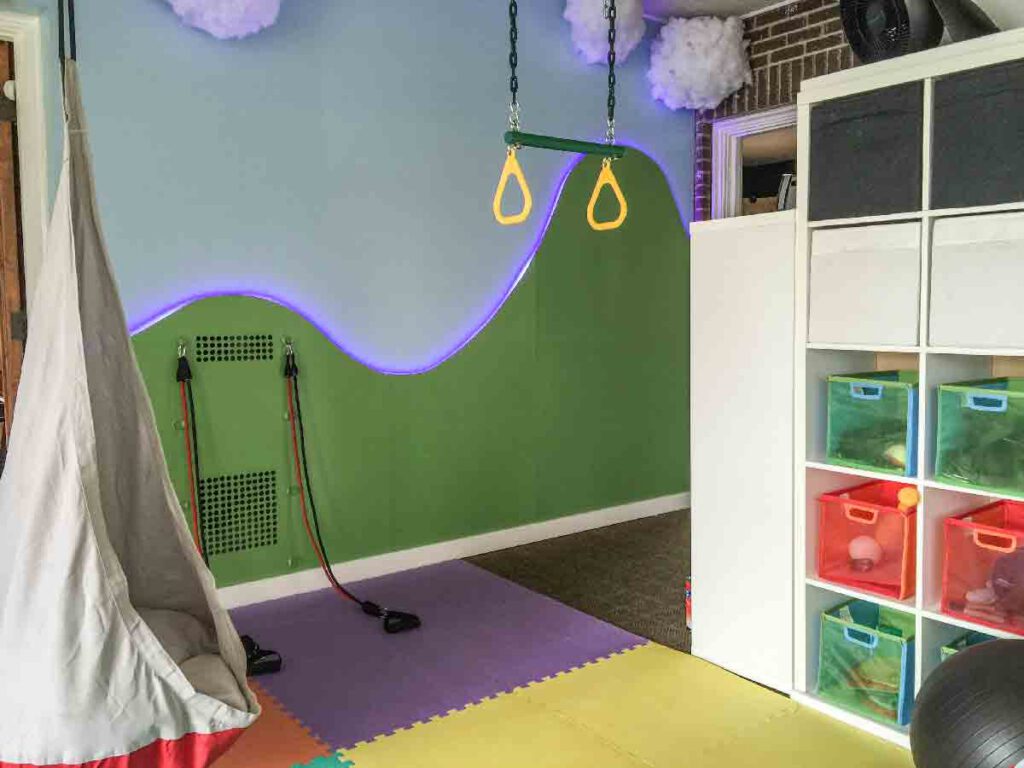 Indoor pediatric gym at Bright Mosaic in Denton featuring a hanging sensory swing, gymnastic rings, resistance bands, and colorful foam flooring for gross motor skill development.