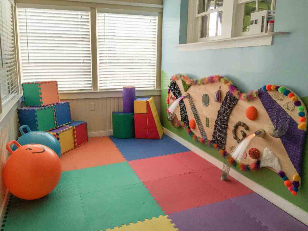Indoor sensory room at Bright Mosaic in Denton featuring colorful foam floor mats, a large tactile wall board with varied textures, and exercise balls for sensory regulation and OT therapy.