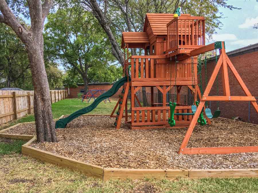 Private, fenced-in wooden playground at Bright Mosaic Autism Center in Denton, featuring a slide, swings, and climbing structure for outdoor sensory play and ABA therapy.
