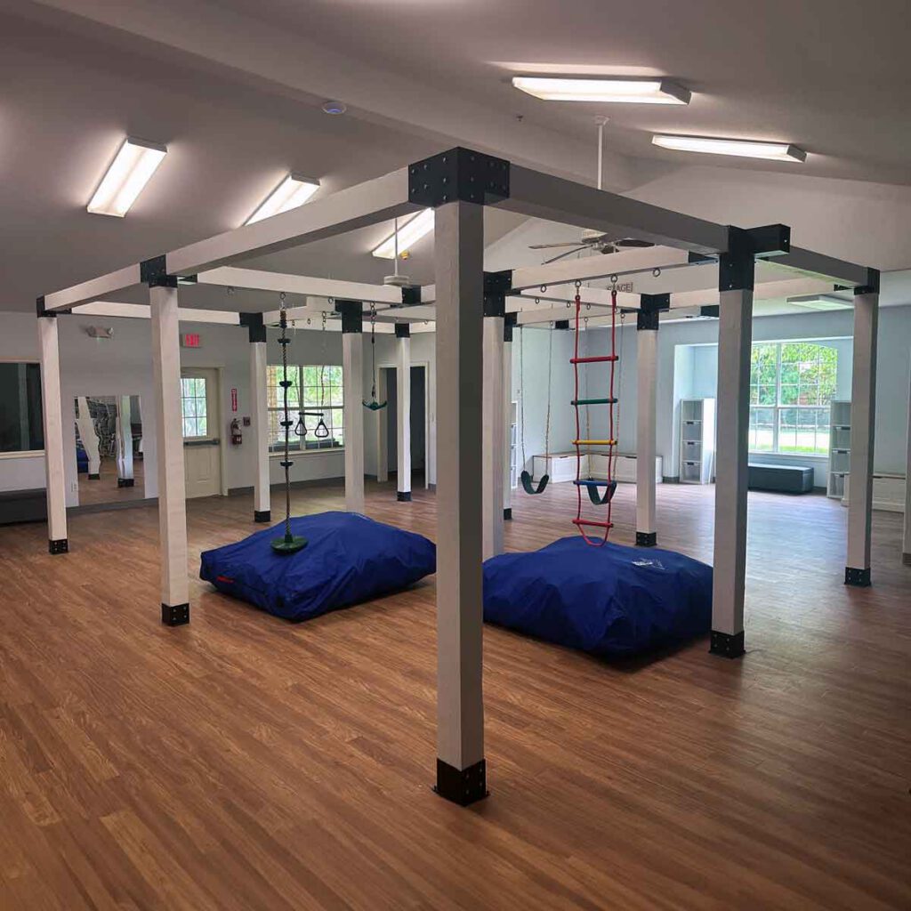 Large, state-of-the-art indoor gym at Bright Mosaic Southlake featuring a custom timber play structure with rope ladders, sensory swings, and crash pads for advanced motor skill development.