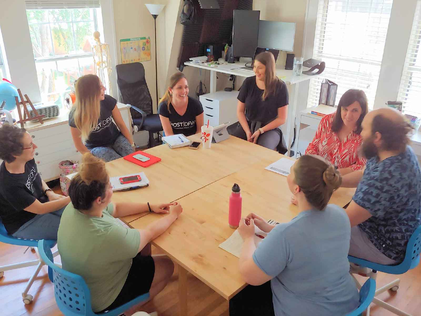 A group of pediatric therapists and parents sitting around a conference table collaborating on child development goals during a caregiver collaboration meeting.