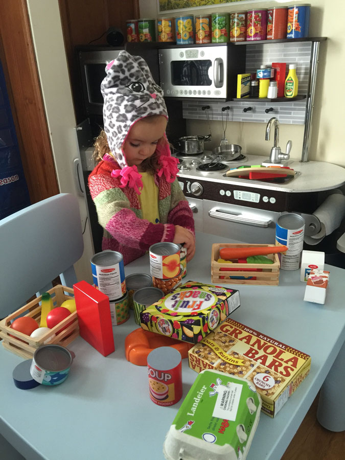 A young girl playing with toy grocery items and a play kitchen during a naturalistic pediatric therapy assessment.