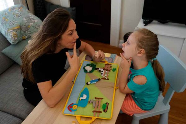 A young girl mirrors her therapist's mouth movements during a individual pediatric speech therapy session.