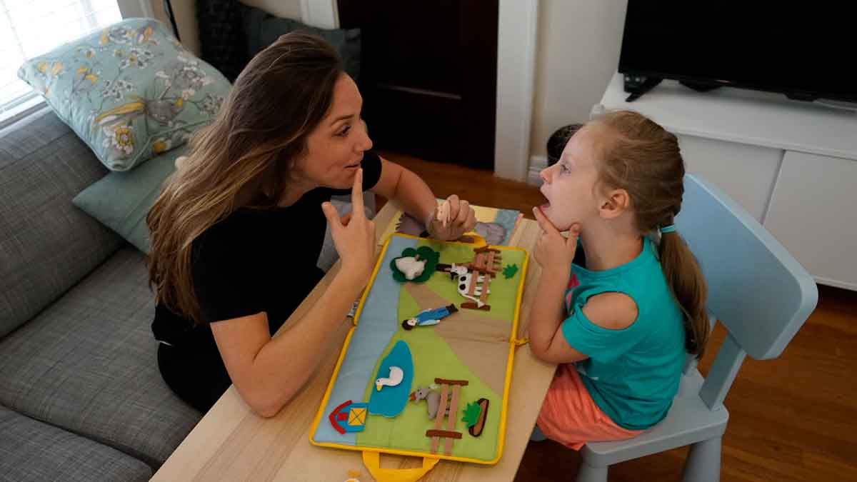 A young girl mirrors her therapist's mouth movements during a individual pediatric speech therapy session.