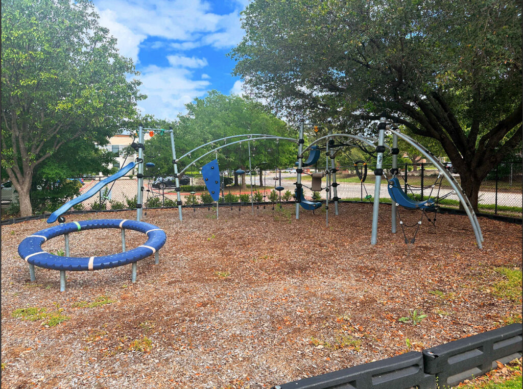 Modern outdoor vestibular playground at Bright Mosaic Southlake featuring a blue circular spinner, arched climbing frames, and sensory-integrated play structures for advanced motor skill development.